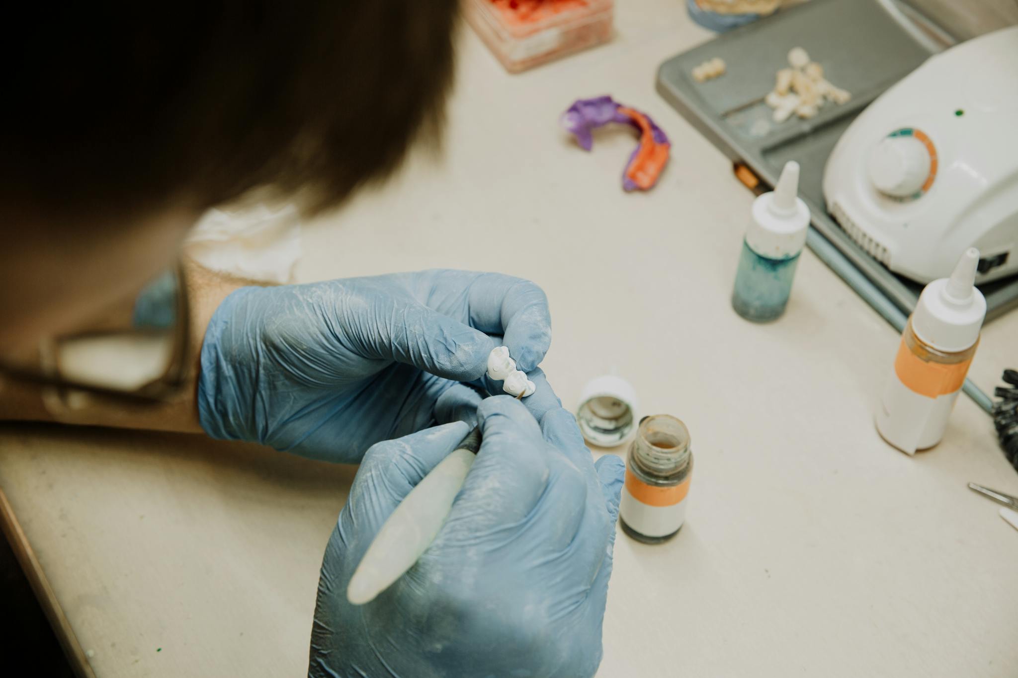 From above of crop anonymous dentist in gloves creating artificial teeth while sitting at table in modern dental laboratory